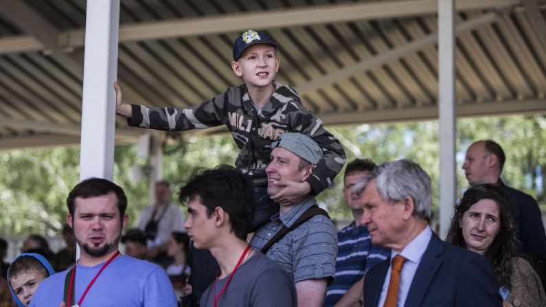  A boy wearing a military sweatshirt watches a tank ride at the theme park.