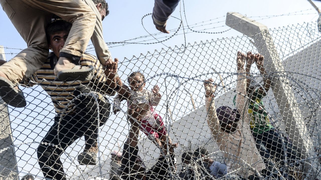 A Syrian child fleeing the war gets lifted over fences to enter Turkish territory illegally near a border crossing at Akcakale, Turkey, on June 14, 2015.