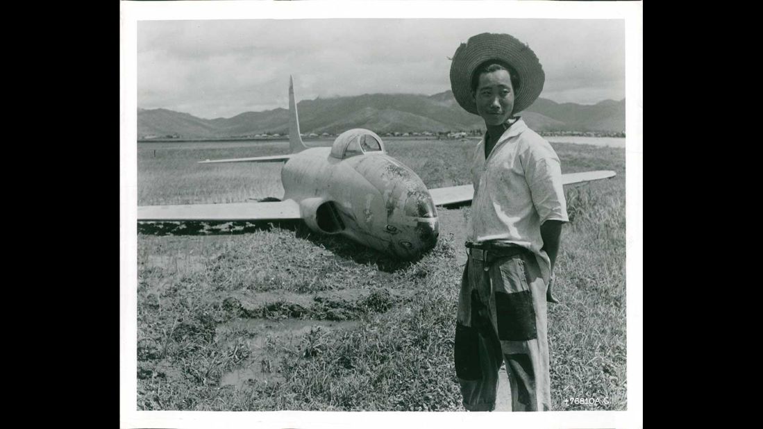 An unidentified farmer stands next to a battle-damaged fighter jet in a South Korean rice field in July 1950. Photo ID: *76810 A.C. 