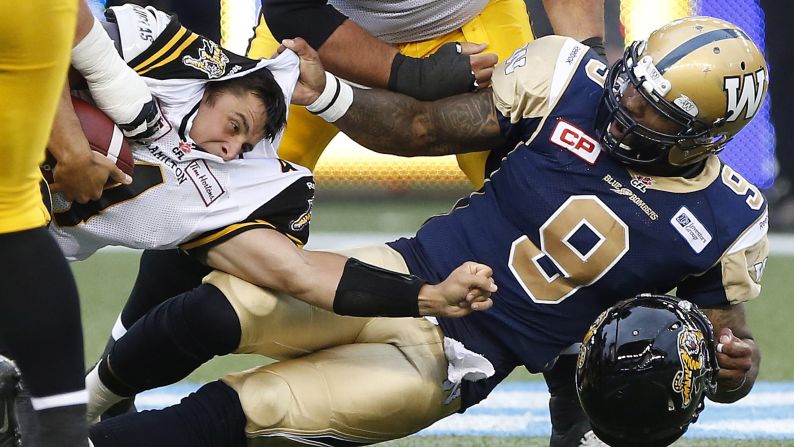 Winnipeg Blue Bombers' Thaddeus Gibson, No. 9, tackles Hamilton Tiger-Cats quarterback Zach Collaros, and later received a penalty for ripping off his helmet, during a Canadian Football League preseason game in Winnipeg, Manitoba, on Friday, June 19.