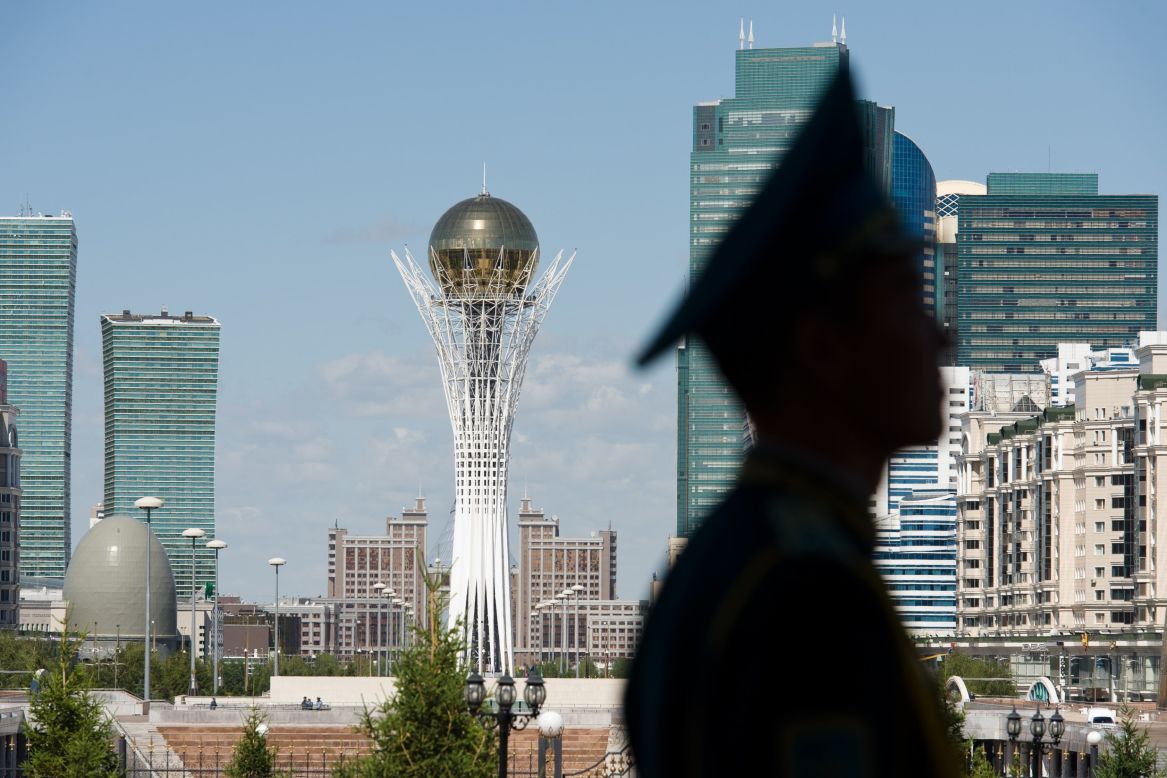 The Bayterek Tower, a monument and viewing tower, is visible in the center of Astana as a soldier stands guard.