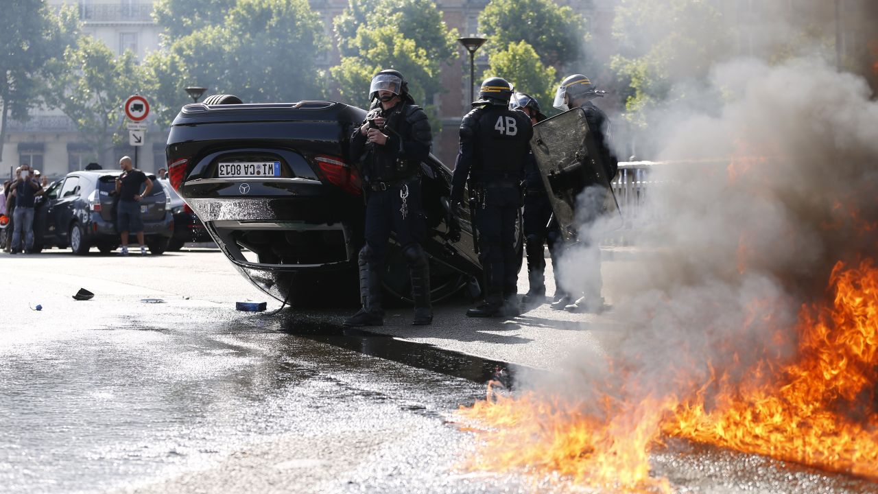 A fire burns next to riot police and an overturned car in Paris on June 25.