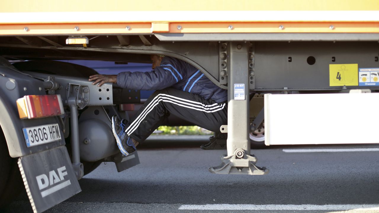 A migrant sits under the trailer of a truck as he attempts to cross the English Channel in Calais, France, on Wednesday, June 24.