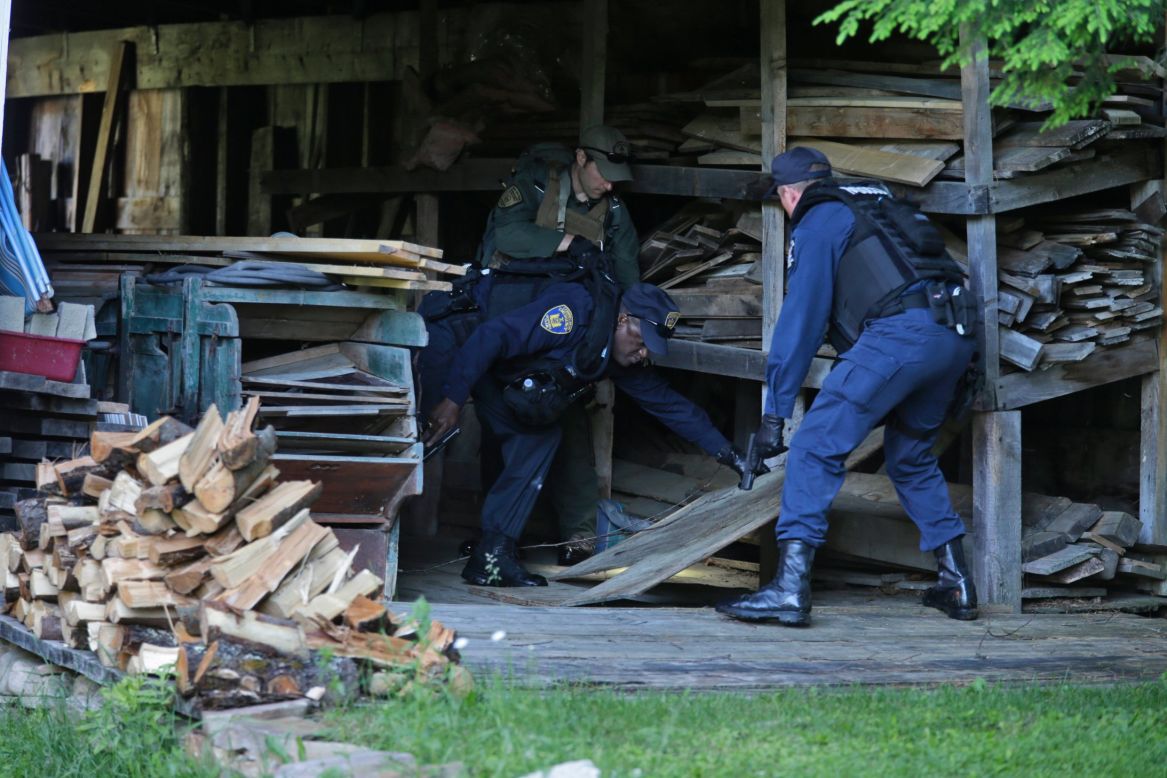 Department of Corrections officers and a forest ranger, back, search a barn in Owls Head, New York, on June 26. 