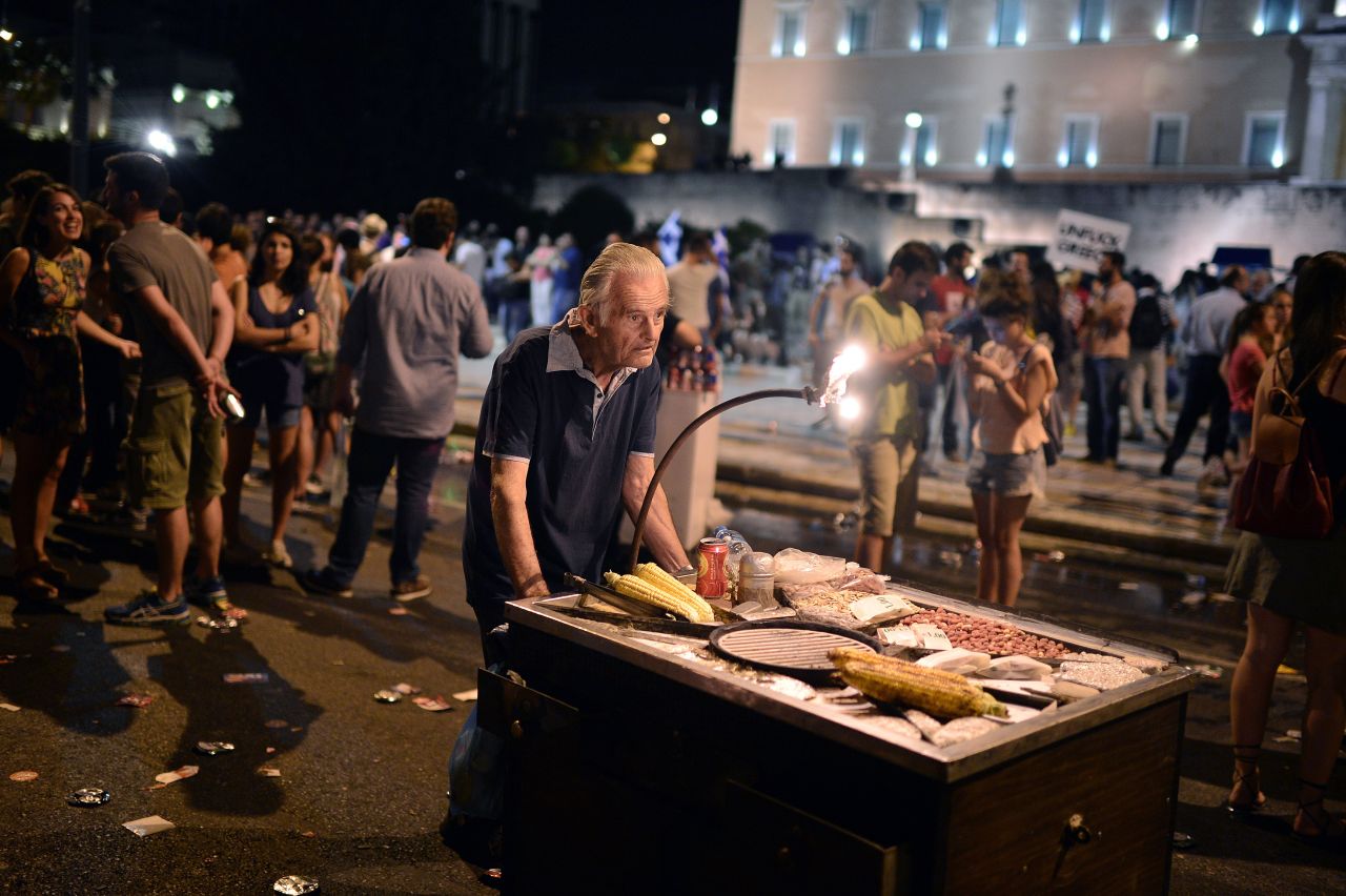 An elderly man pushes a cart with corn for sale as people celebrate the victory of the 'no' campaign in front of the parliament.