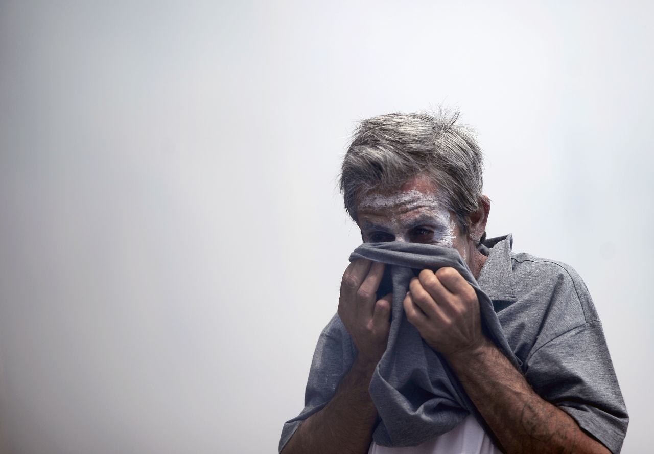 A demonstrator protects his face from teargas thrown by riot police. 