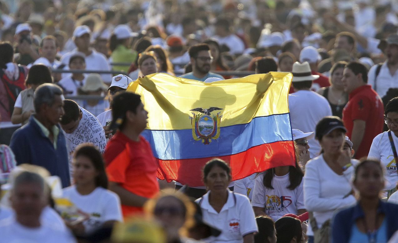 A woman holds up an Ecuadorian flag in a crowd of people waiting in Guayaquil on July 6. More than 1 million were expected to attend the Mass. Many camped out overnight.