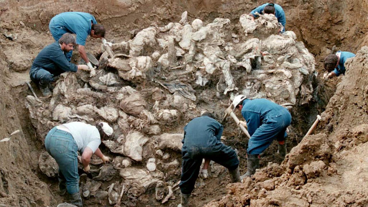 Investigators and forensic experts work on top of a cluster of bodies, many of them with their hands tied in the back and many of them blindfolded