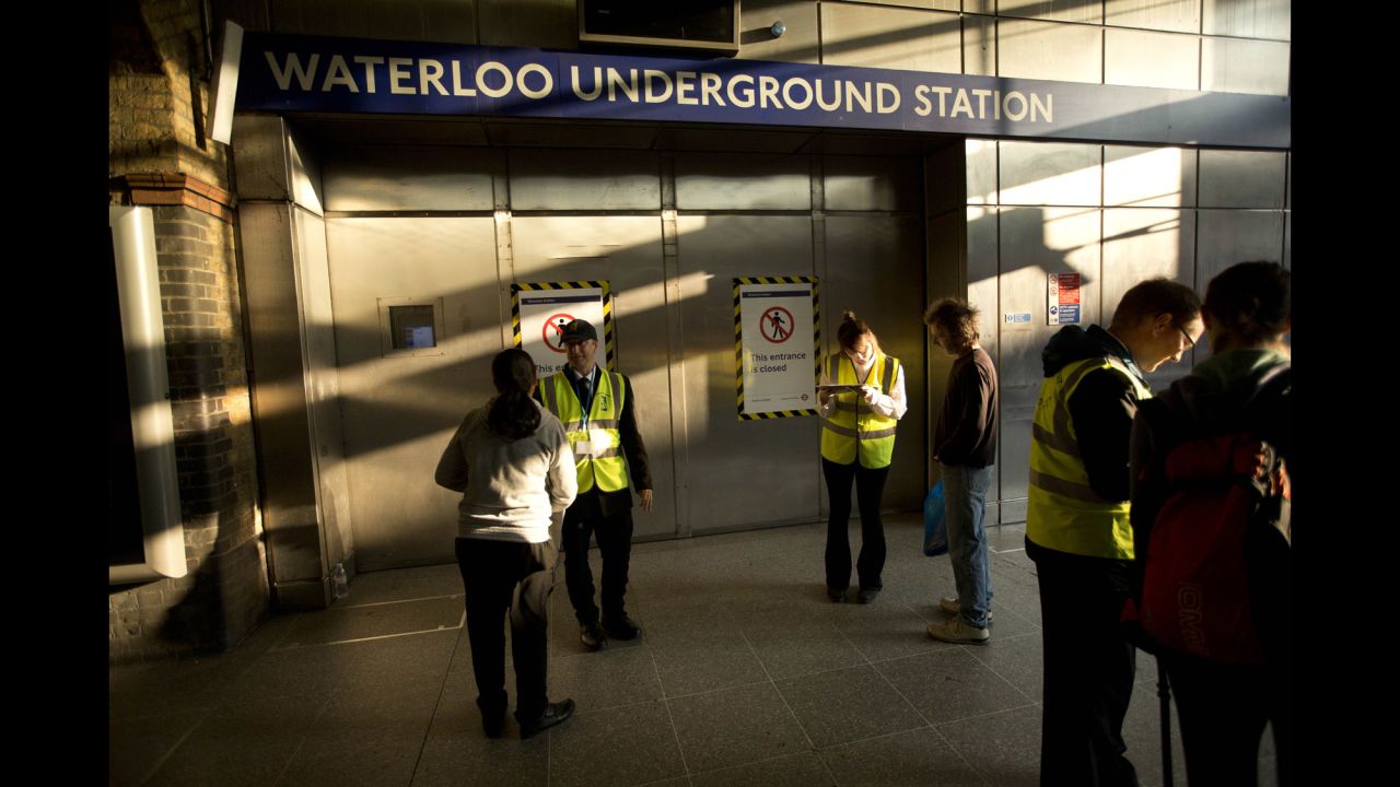 Workers from an outside agency give people travel advice by the closed entrance doors of the Waterloo Underground train station in London on July 9.