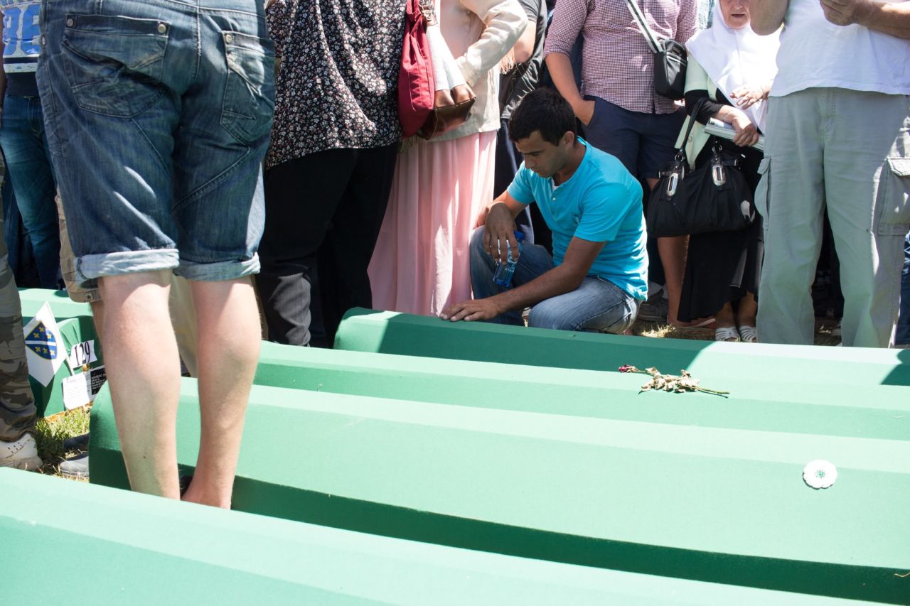 A man sits next to one of 136 coffins with newly discovered or identified remains waiting to be buried.