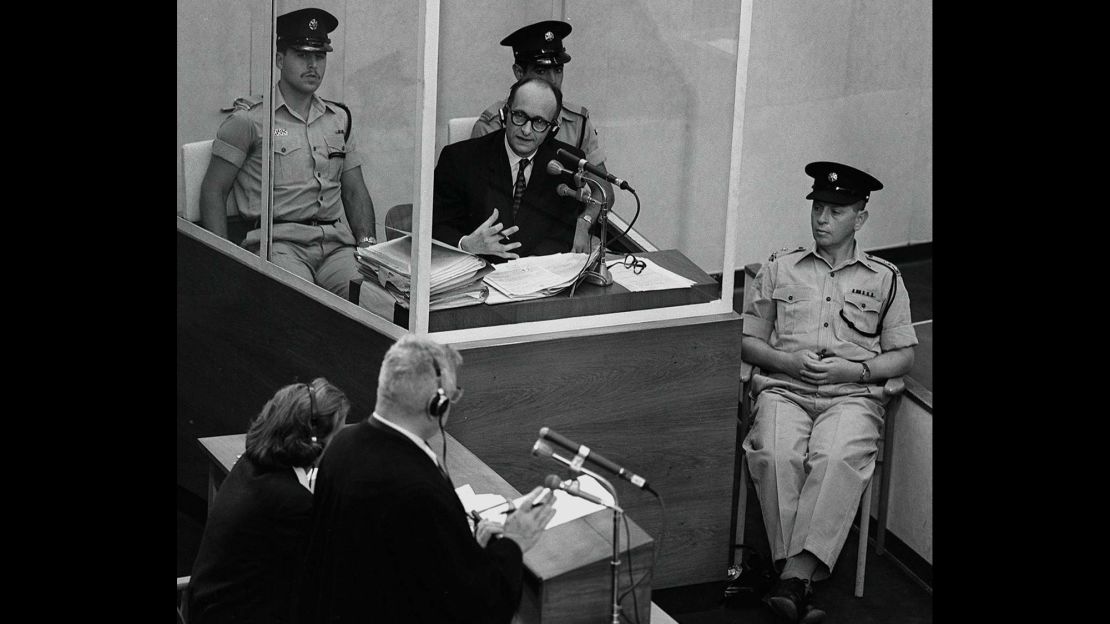 Eichmann stands in a protective glass booth flanked by Israeli police during his 1961 war crimes trial.