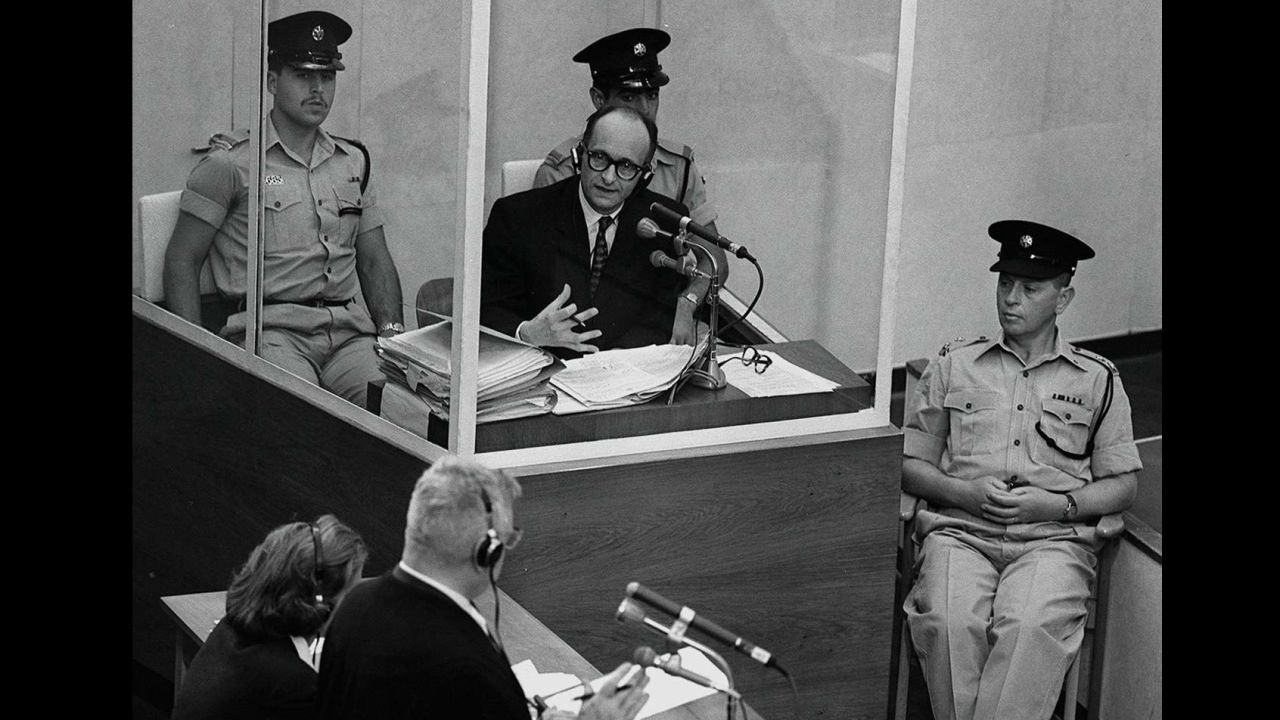 Eichmann stands in a protective glass booth flanked by Israeli police during his 1961 war crimes trial.