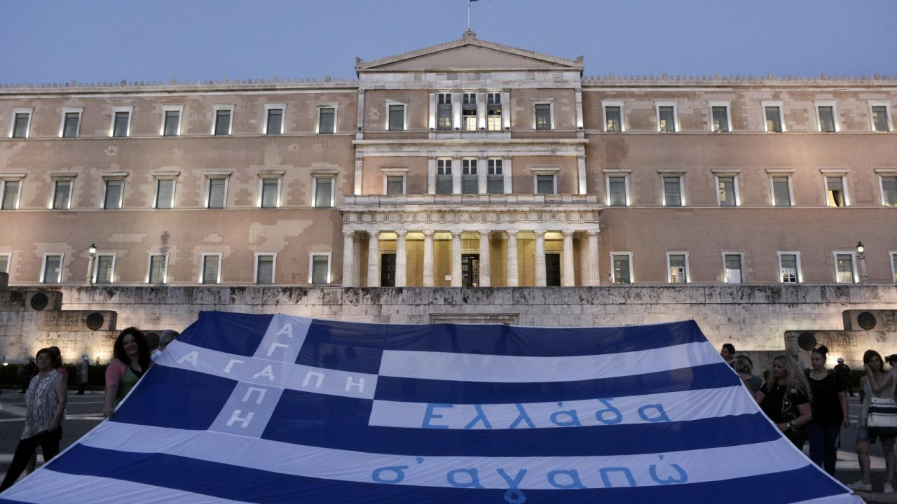 Demonstrators display the Greek flag in front of parliament on July 15, 2015 in Athens, Greece. Anti-austerity protesters hurled petrol bombs at police in front of Greece's parliament as lawmakers began debating deeply unpopular reforms needed to unlock a new eurozone bailout. Riot police responded with tear gas against dozens of hooded protesters who set ablaze parts of Syntagma square in central Athens.