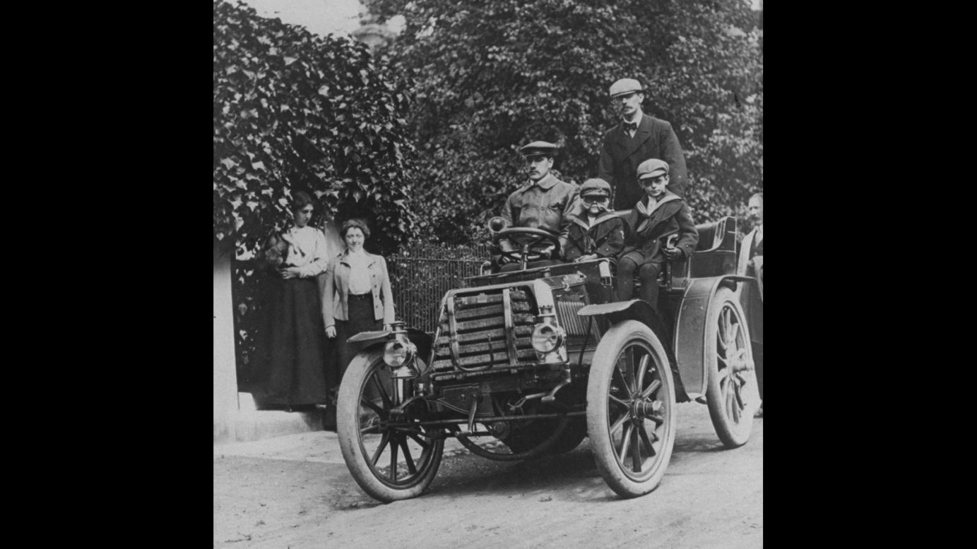 Ford's 1903 Model A, with a base price of $750, was enough of a success to allow the company to grow. Here, a family proudly sits in one while women look on from the side of the road. 