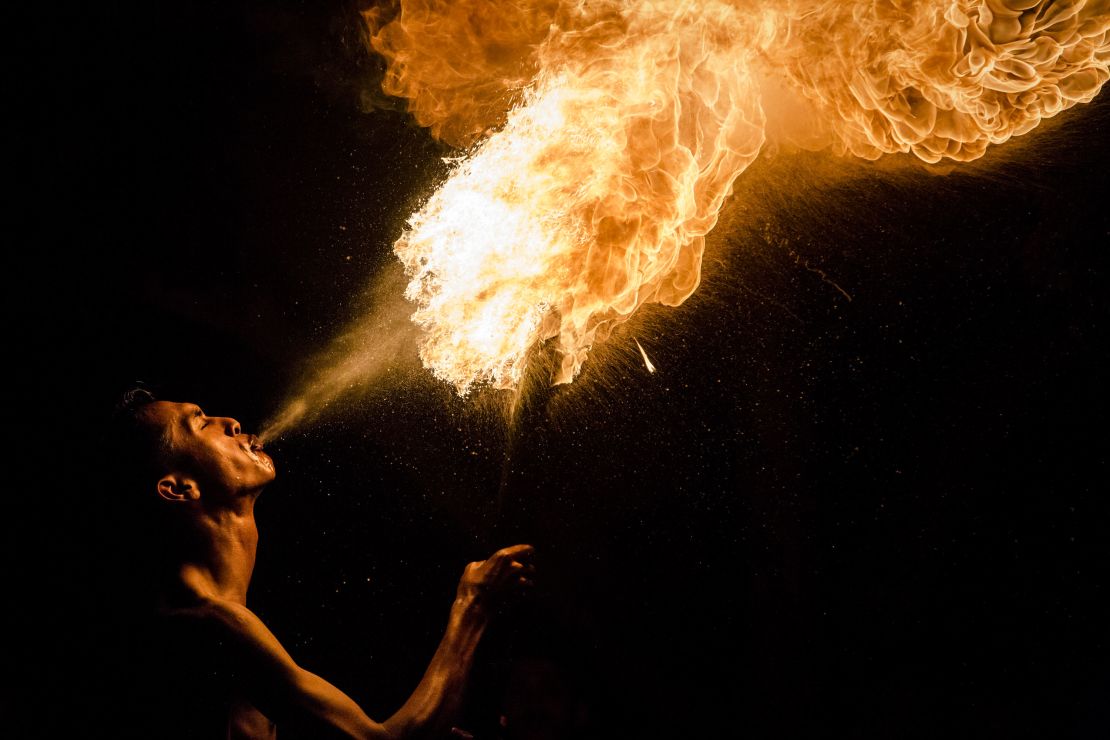 A Muslim man breathes fire during a game of fire football, known as "bola api."