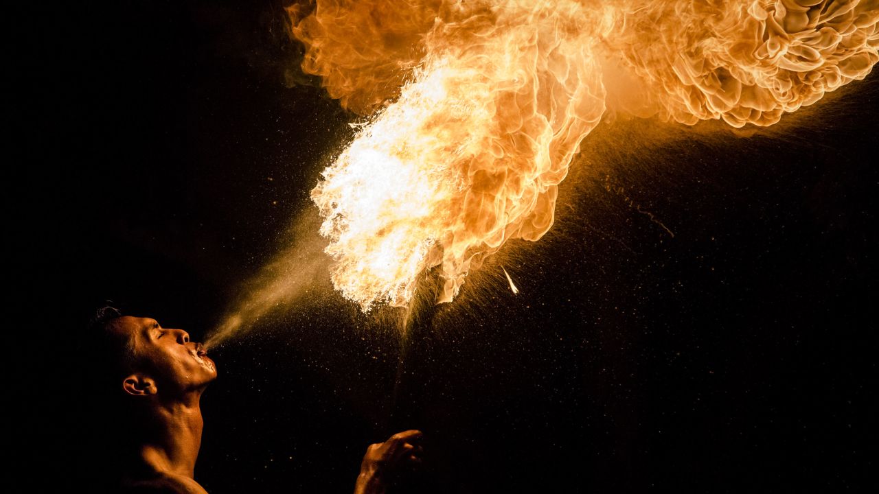 A Muslim man breathes fire during a game of fire football, known as "bola api."