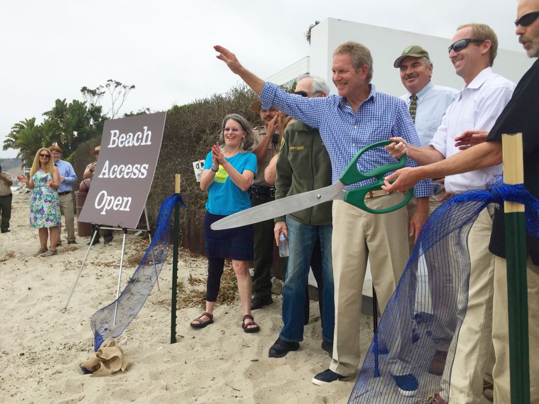 Steve Kinsey waves and Aaron McClendon and Charles Lester, right, wield giant scissors as the Coastal Commission officials formally open the path.