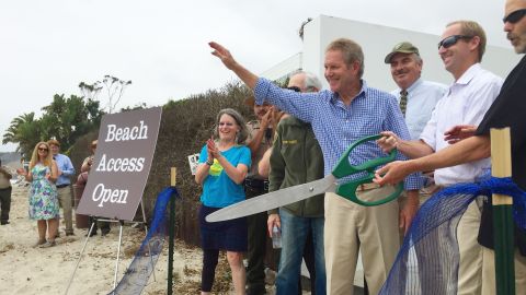 Steve Kinsey waves and Aaron McClendon and Charles Lester, right, wield giant scissors as the Coastal Commission officials formally open the path.