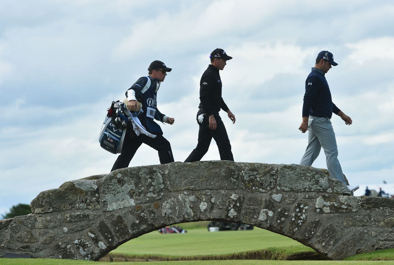 Gary Woodland of the United States (R), Danny Willett of England (C) and his caddie Jonathan Smart (L) walk across Swilcan Bridge.