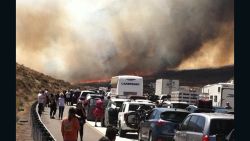 Bystanders look on along Interstate 15 on the Cajon Pass, Friday, July 17, 2015, near San Bernadino, Calif., as a fast-moving wildfire swept across the Southern California freeway, destroying numerous vehicles and sending motorists running to safety before burning at least five homes. (Arsenio Alcantar via AP)