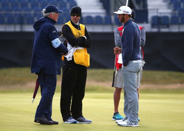 Open Championship leader Dustin Johnson talks with a rules official on the 15th green as play is suspended due to high winds early on Saturday morning.