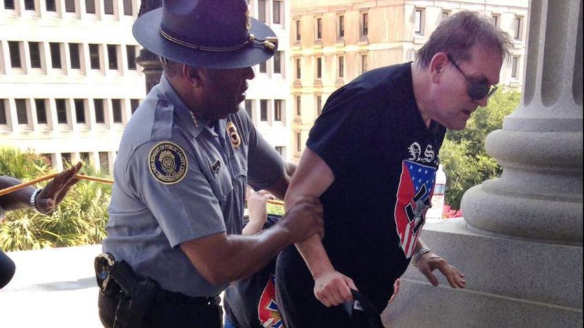 In this photo provided by Rob Godfrey, police officer Leroy Smith, left, helps a man wearing National Socialist Movement attire up the stairs during a rally Saturday, July 18, 2015, in Columbia, S.C. Members of the group were protesting Saturday the removal of the Confederate flag from the Statehouse grounds earlier this month. (Rob Godfrey via AP)