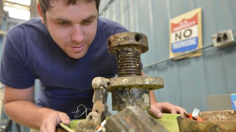 Parker Brooks, a conservator and graduate student at Texas A&M University, studies an elevator screw and firing mechanism from a CSS Georgia cannon.