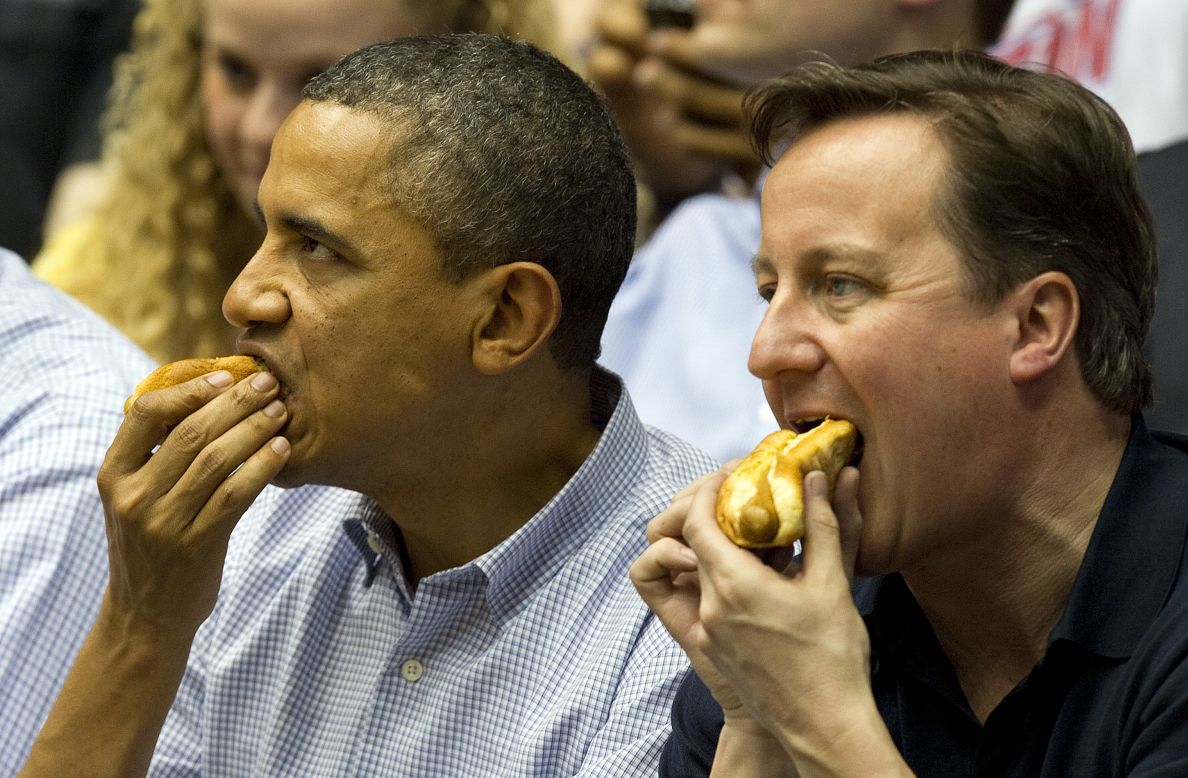 U.S. President Barack Obama and British Prime Minister David Cameron eat hot dogs as they sit in the stands at University of Dayton Arena in Dayton, Ohio, on March 13, 2012, while attending the NCAA Division I Men's Basketball Championship First Four.