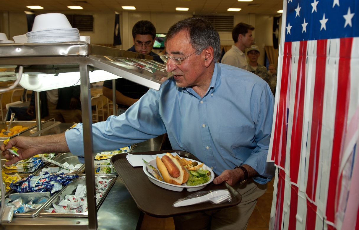Then-U.S. Secretary of Defense Leon Panetta reaches for a packet of mustard and relish as he takes a hot dog for lunch during his visit to Camp Victory in Baghdad on July 11, 2011.