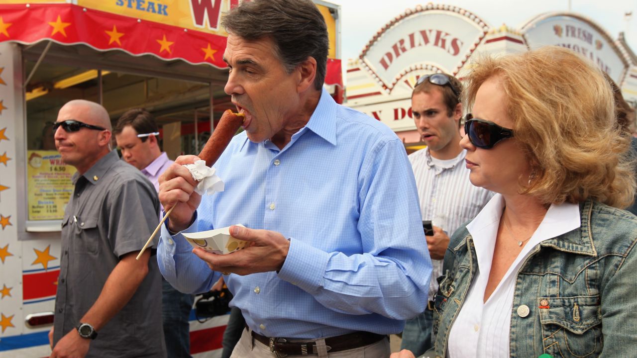 Republican presidential candidate and Texas Governor Rick Perry eats a 'veggie' corn dog and walks with his wife Anita while visiting the Iowa State Fair August 15, 2011 in Des Moines, Iowa. 