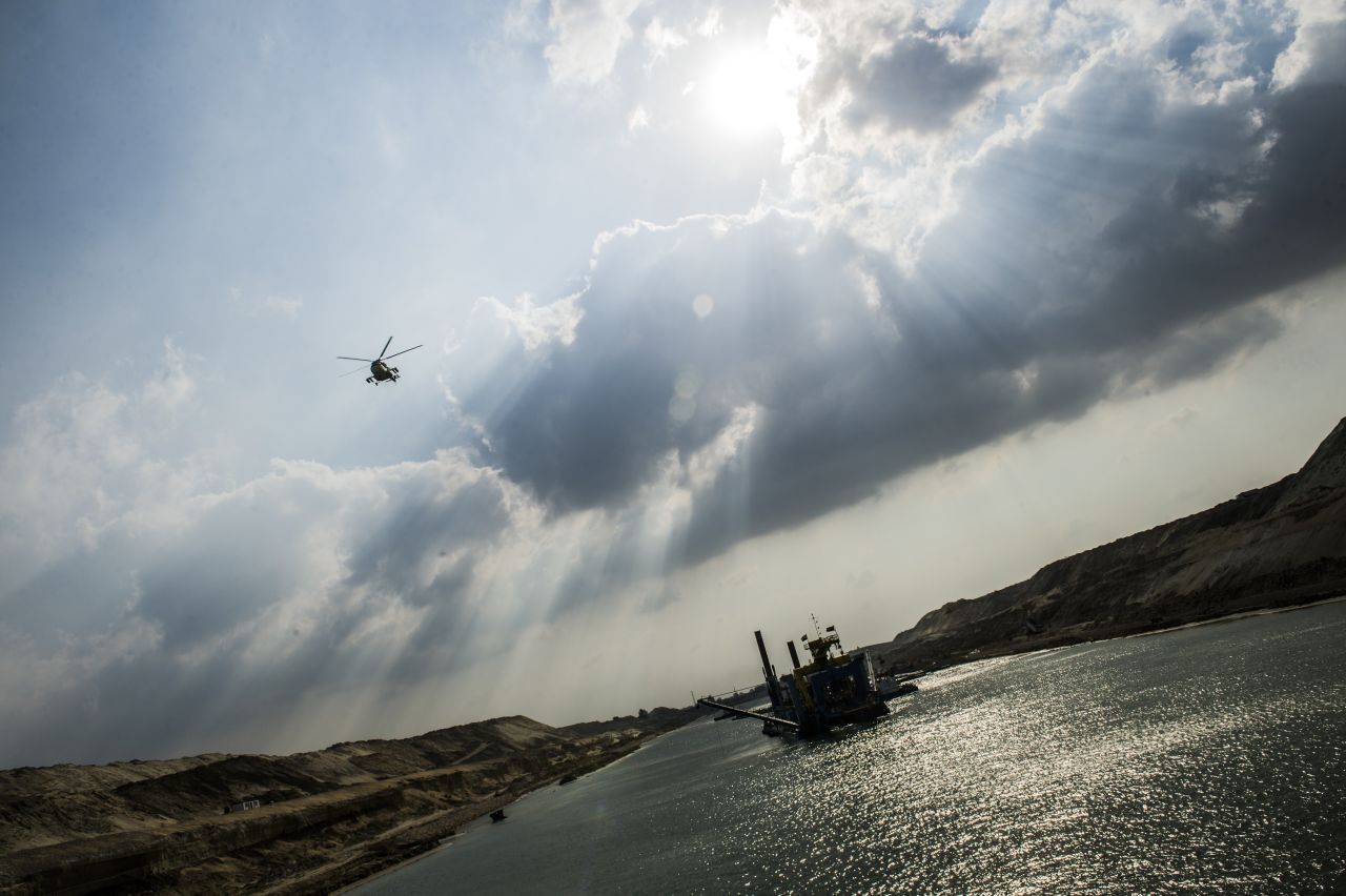 An Egyptian army helicopter flies over a dredger at work on the new waterway of the Suez Canal on June 13, 2015, in the port city of Ismailia, east of Cairo. The government hopes the ambitious industrial project will generate $100 billion in revenue and create 1 million jobs.