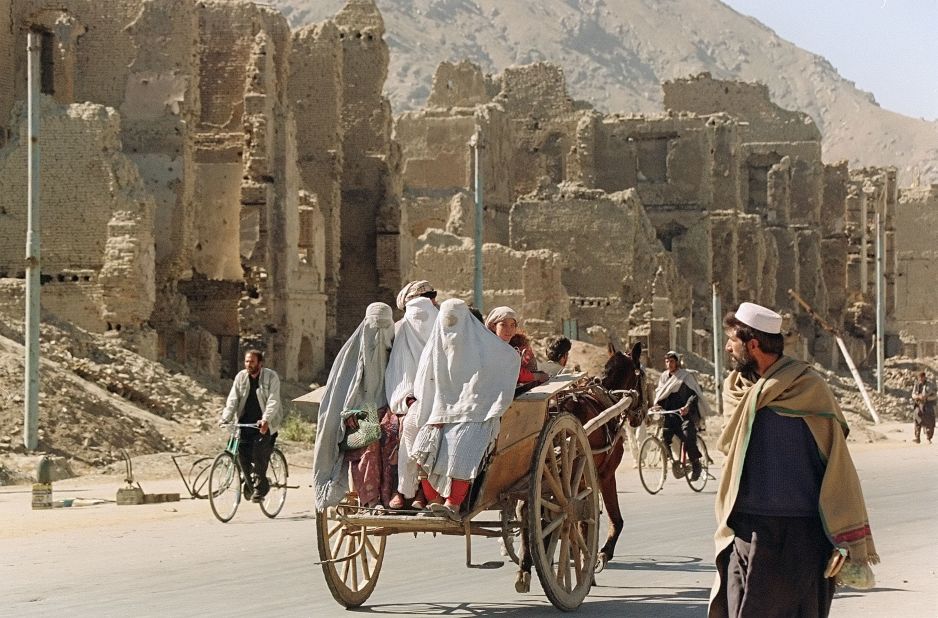 Three women hitch a ride on the back of a donkey cart as they pass by the ruins of Kabul's former commercial district in November 1996.
