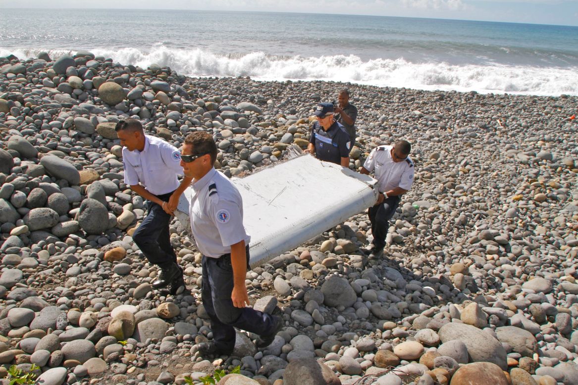 French police officers carry the plane debris on July 29. Experts say the metallic object may be a piece of a moving wing surface, known as a flaperon, from a Boeing 777.