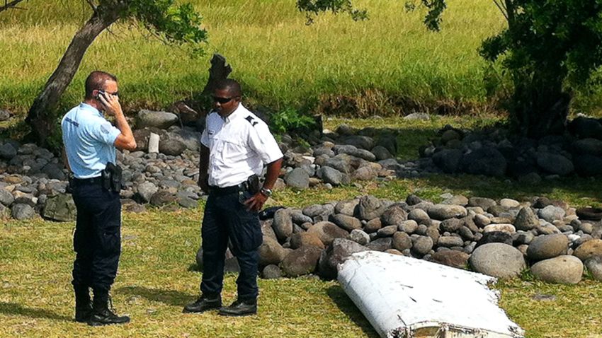 A policeman and a gendarme stand next to a piece of debris from an unidentified aircraft found in the coastal area of Saint-Andre de la Reunion, in the east of the French Indian Ocean island of La Reunion, on July 29, 2015.