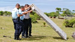 In this photo dated Wednesday, July 29, 2015, French police officers inspect a piece of debris from a plane in Saint-Andre, Reunion Island. Air safety investigators, one of them a Boeing investigator, have identified the component as a "flaperon" from the trailing edge of a Boeing 777 wing, a U.S. official said. Flight 370, which disappeared March 8, 2014, with 239 people on board, is the only 777 known to be missing. (AP Photo/Lucas Marie)
