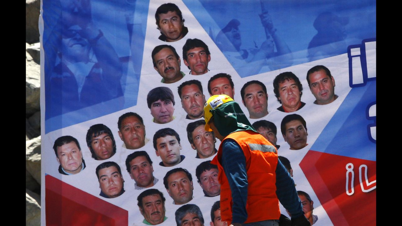 A rescue worker walks past a banner with pictures of the trapped miners on October 11.