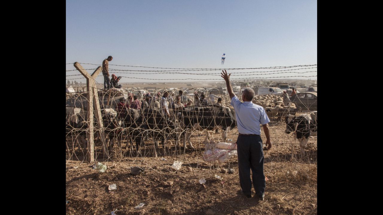 A Turkish man throws a bottle of water across the barbed-wire border fence to a Syrian man waiting on the other side.