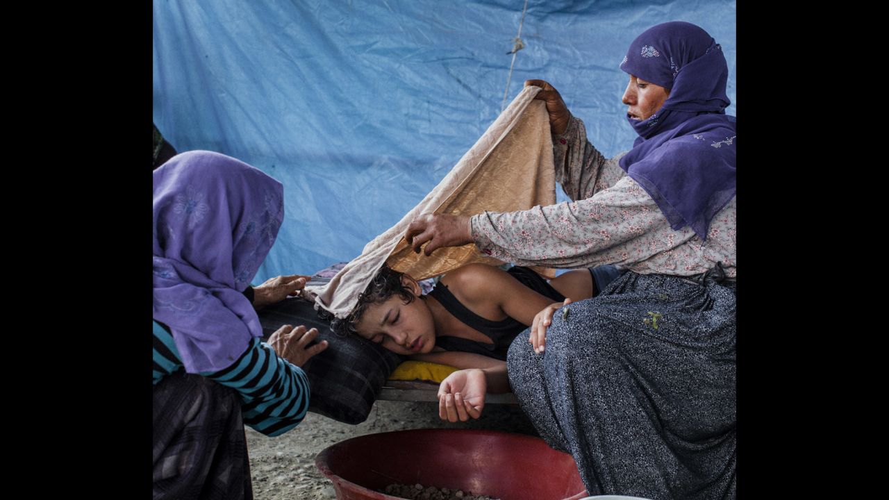 Nizal, 14, is tended to by his mother and a relative after falling ill. The family was living in a small tented area on the outskirts of Adana in southern Turkey.