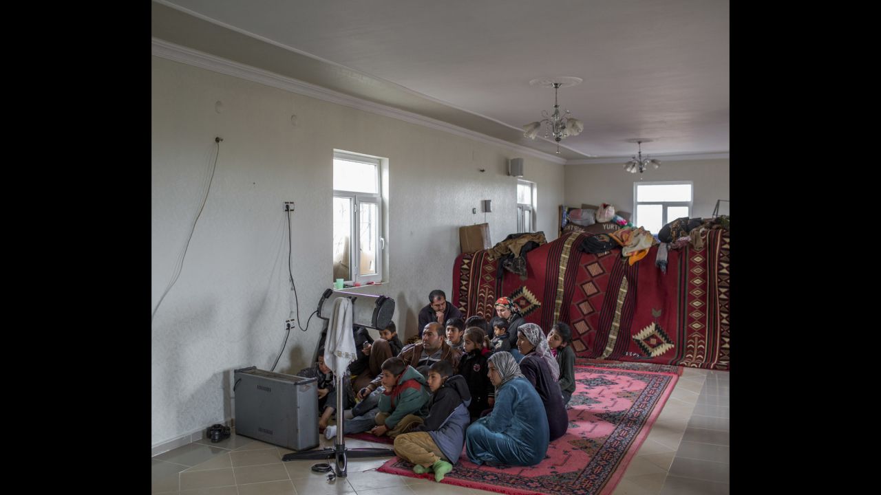 A family of Syrian refugees huddle around the heater while watching television in the unfinished building where they have found refuge in Turkey.