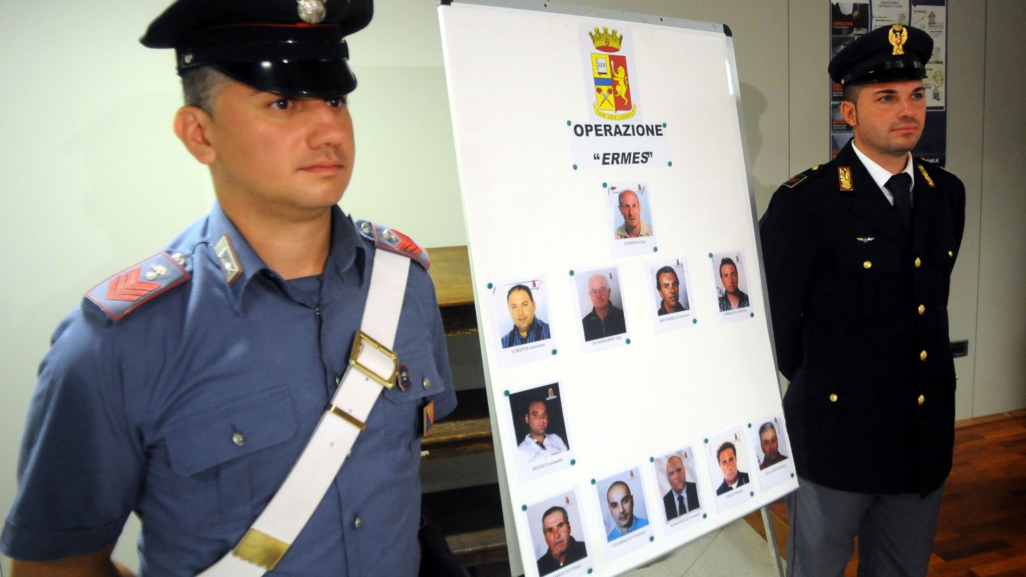 Italian authorities stand next to mugshots of 11 men suspected of helping Matteo Messina Denaro.