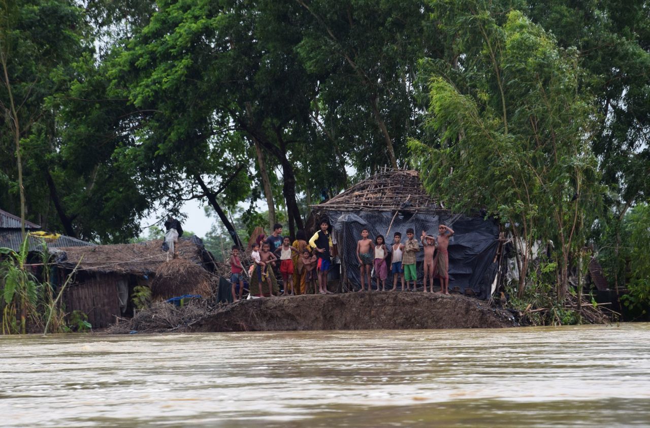 Bangladeshi villagers stand near a broken embankment, avoiding floodwater, in Cox's Bazar on August 2, 2015, after the area was hit by torrential rains from Cyclone Komen. 