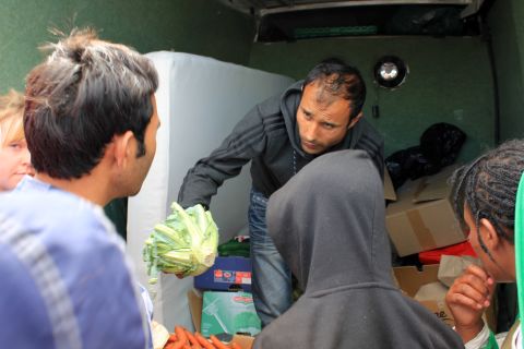 A local charity hands out food. People cover up their faces when the cameras are around because they don't want their families at home to see them in these conditions. Many people tell their families they are doing well in Europe.
