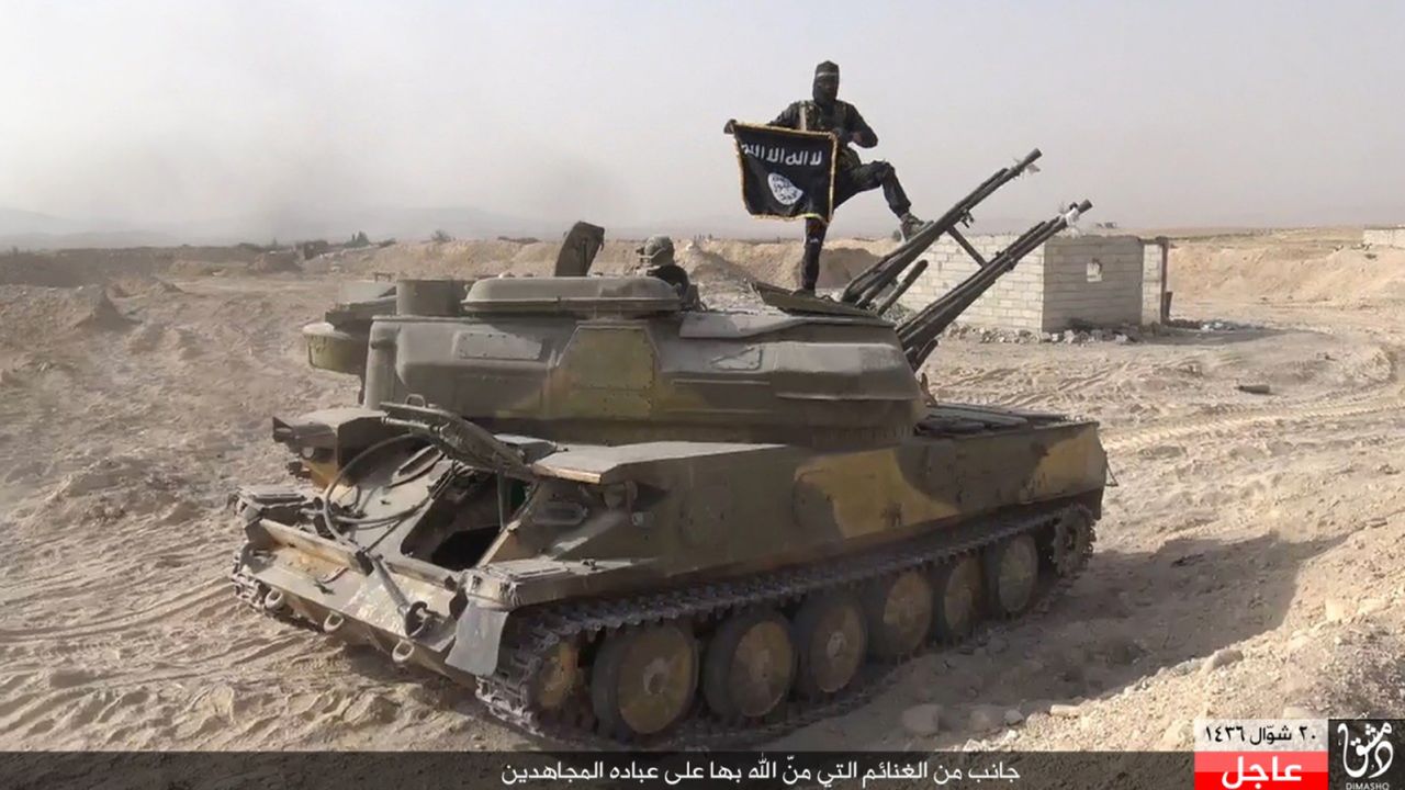 In this image taken from social media, an ISIS fighter holds the group's flag as he stands on a tank.