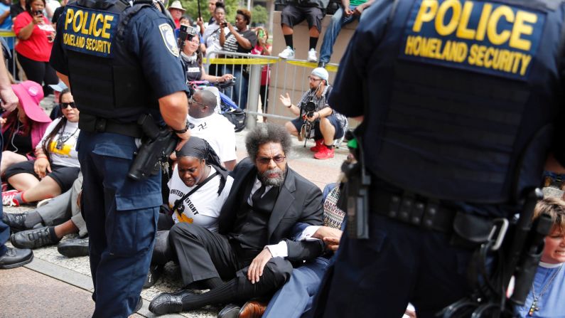 Cornel West, center, joins other protesters sitting on the steps of the Thomas F. Eagleton Federal Courthouse as members of the Federal Protective Service stand watch August 10 in St. Louis. Protesters have been arrested after blocking the entrance to the courthouse while calling for more aggressive U.S. government response to what they call racist law enforcement practices. 