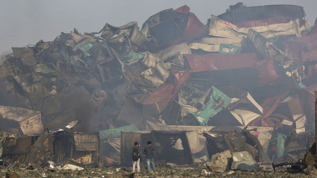 People walk among the crumpled remains of shipping containers. One of the explosions was estimated to be equivalent to 21 tons of TNT, or a magnitude-2.9 earthquake, according to the China Earthquake Networks Center.