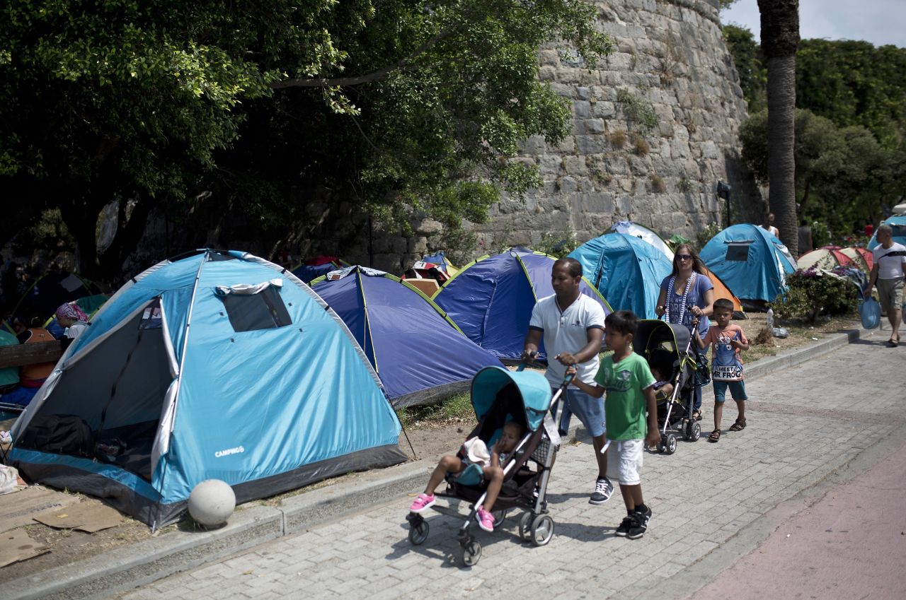 People walk past tents of migrants set up in the street on August 10.