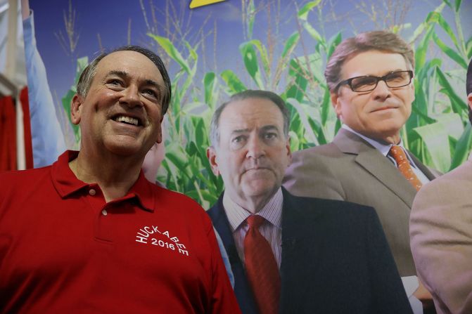 Former Arkansas Gov. Mike Huckabee stands next to a poster featuring all of the Republican candidates as he tours the fair on August 13.