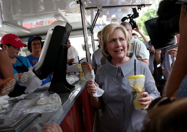 Clinton holds a lemonade and a pork chop on a stick on August 15.