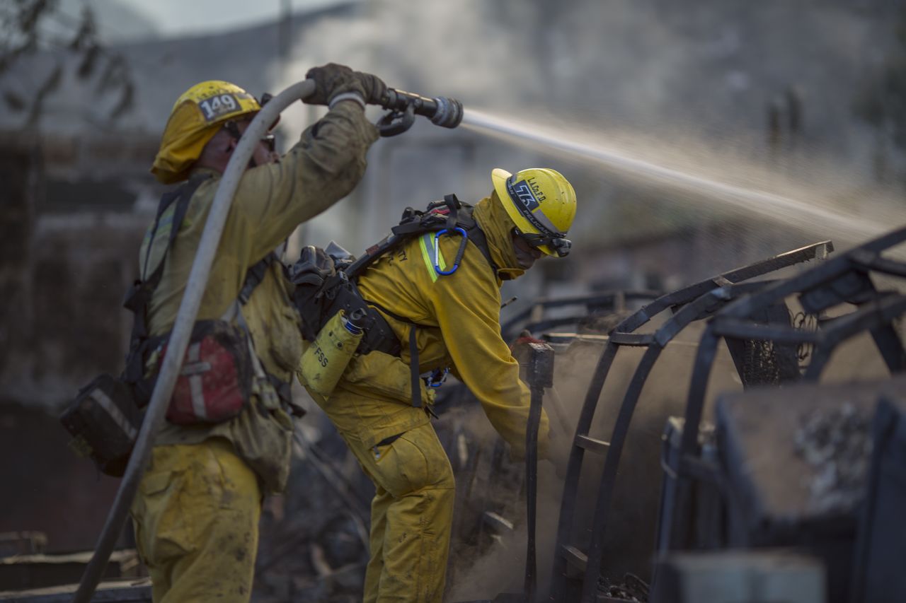 Firefighters hose down the smoldering ruins of a building that was burned by the Warm Fire north of Castaic, California, on Sunday, August 16.