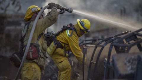 Firefighters hose down the smoldering ruins of a building that was burned by the Warm Fire north of Castaic, California, on Sunday, August 16.